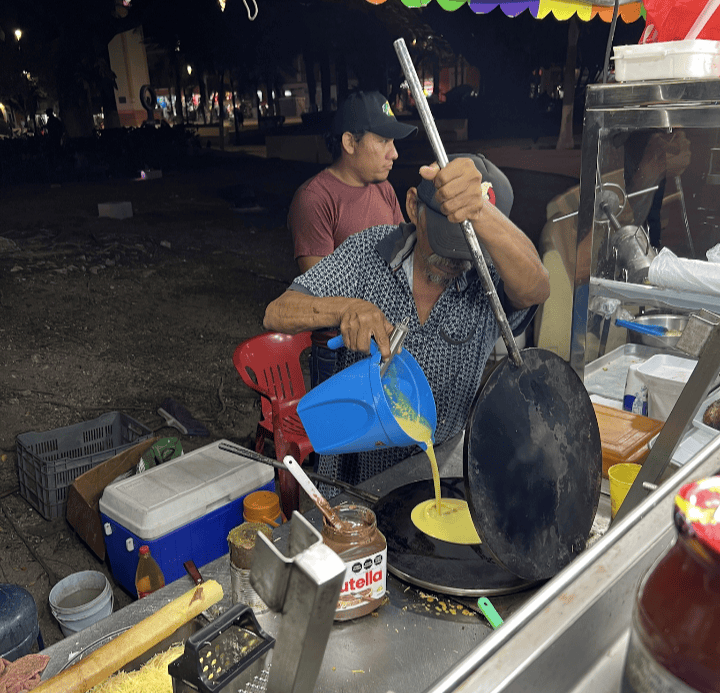 A Cozumel street food vendor pouring egg batter onto a skillet