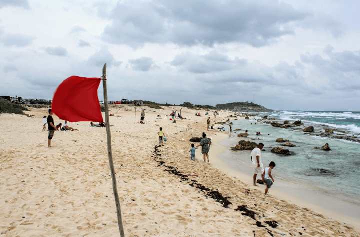 Photo of beach warning flag in Cozumel with beach in background and people on the beach