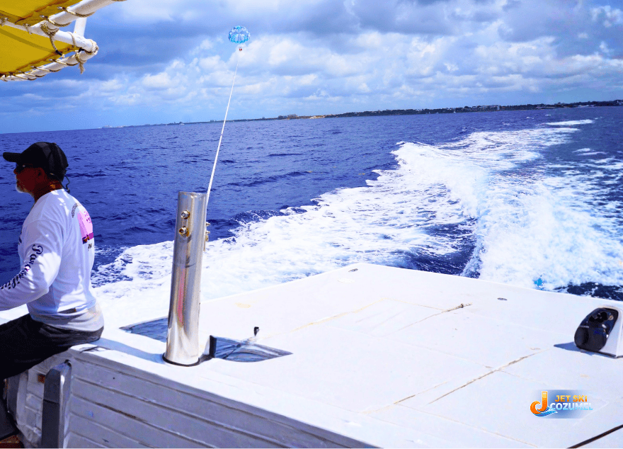 Parasailing Cozumel prices for tours. A Paradailin instructor driving the boat and watching a tandem Parasail on a fully extended line simultaneously