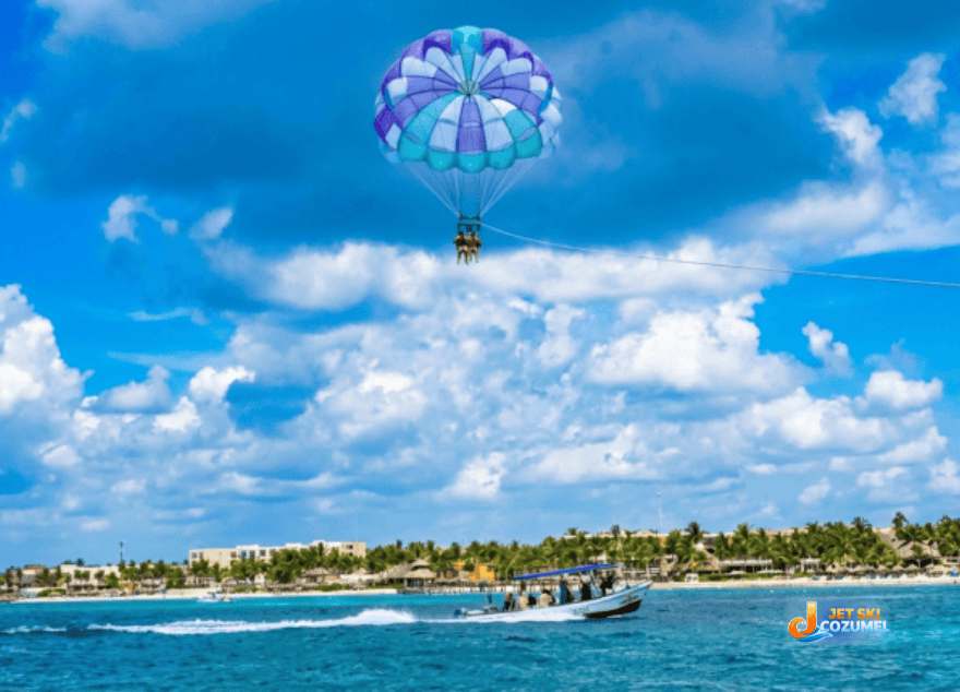 A Cozumel Parasailing tour safety demonstration of a tandem Parasail 200 ft above the water with a boat driving underneath. Cozumels beach in the background