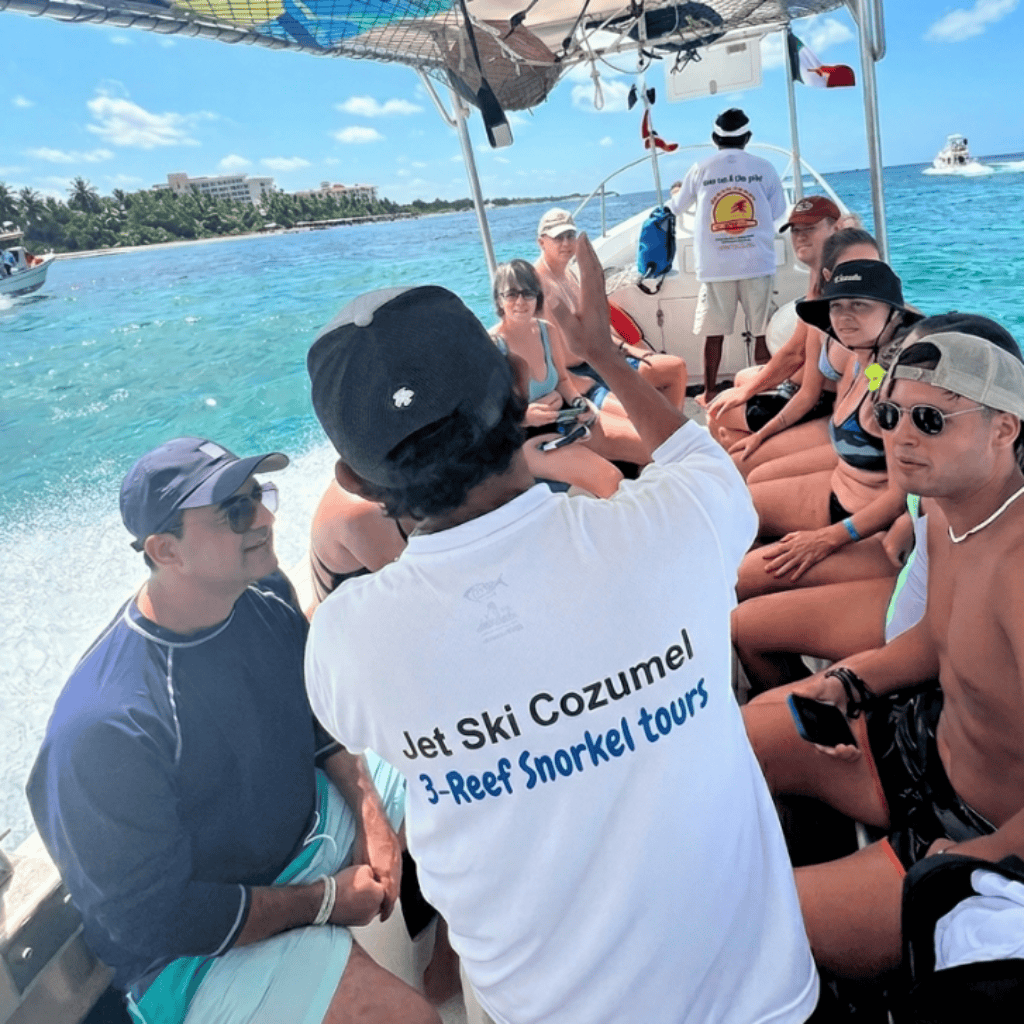 Tour boat full of passengers preparing for a snorkeling trip in turquoise water with palm trees in the background and a guide in a white shirt with Jet Ski Cozumel text