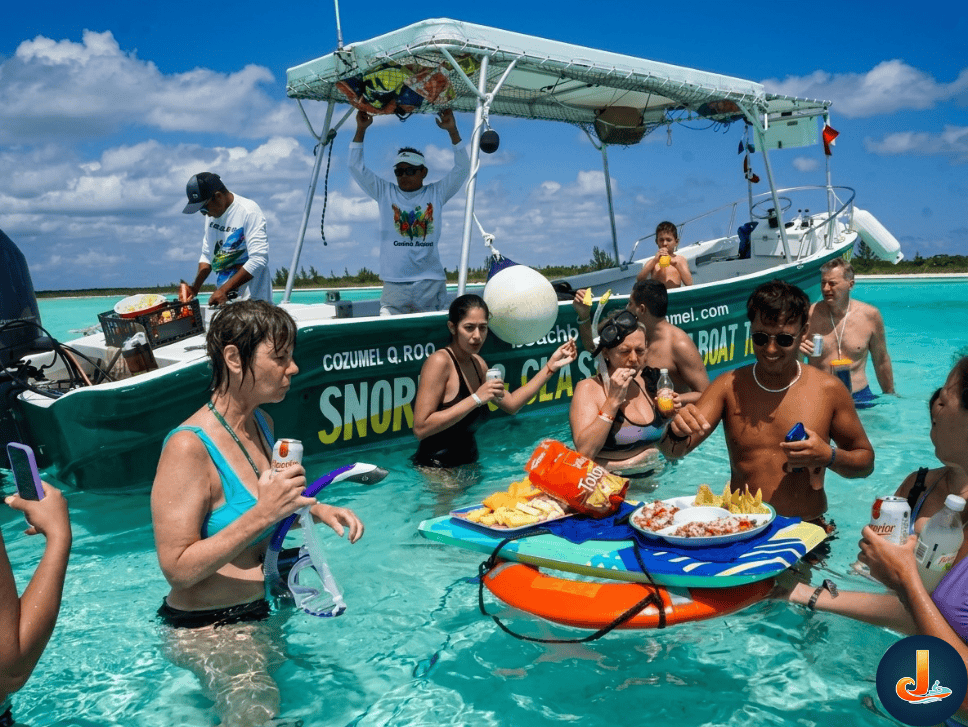 el-cielo-sandbar-snorkelers-experience – Jet Ski Cozumel A group of people standing in clear waist deep water eating chips and salsa pff a floating tray with the snorkel boat on the background at El Cielo sandbar