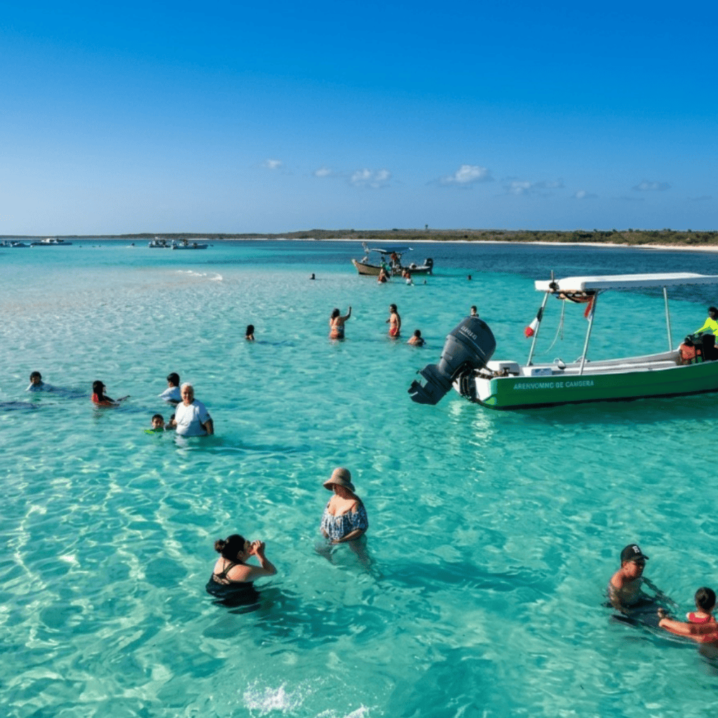 Group of people swimming and wading in clear turquoise water near a green motorboat anchored close to a sandy beach.