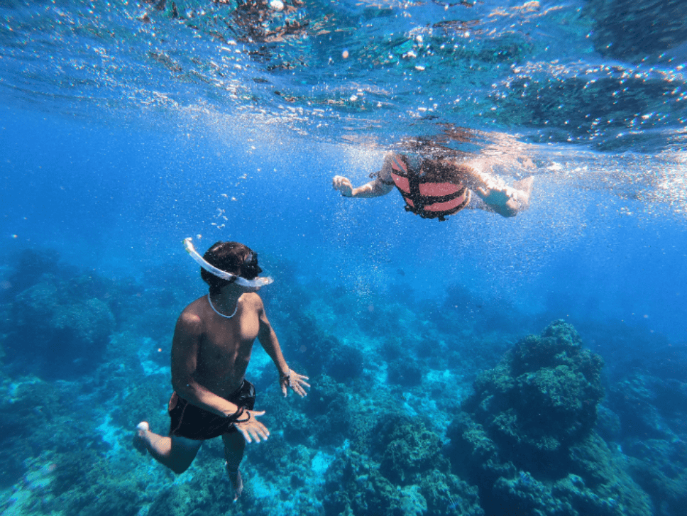 top Cozumel snorkeling spots – Jet Ski Cozumel Two snorkelers exploring a vibrant coral reef underwater; one wears a mask and snorkel, the other near the surface in a pink life vest.